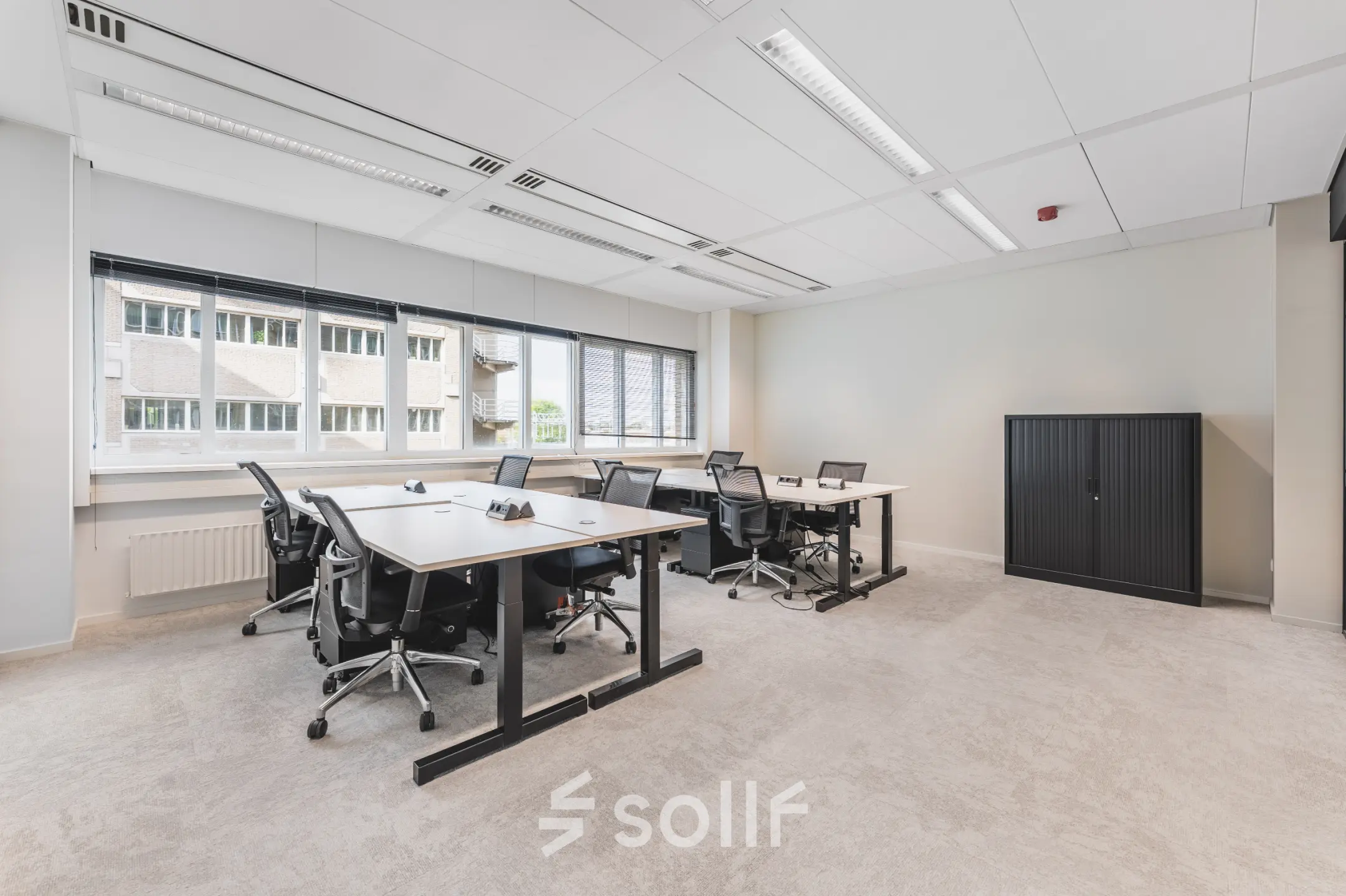 Lichte kantoorruimte met meerdere bureaus en stoelen, grote ramen en een uitzicht op een naastgelegen gebouw, ideaal voor kantoorruimte huren in Utrecht Centraal Station.