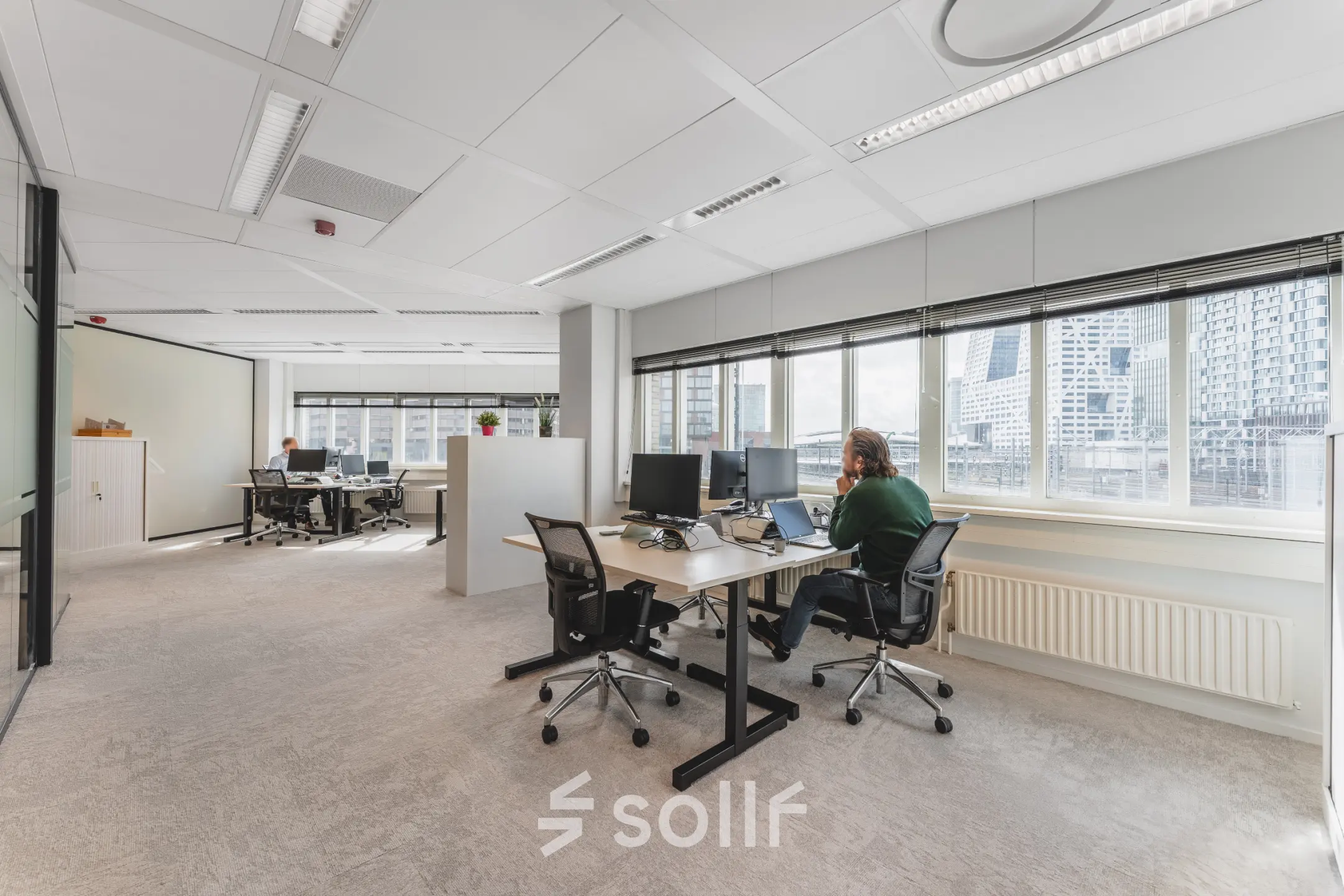 Kantoorruimte op Leidseveer 2-10 bij Utrecht Centraal Station met bureaus, stoelen en computers, waar mensen aan het werk zijn.