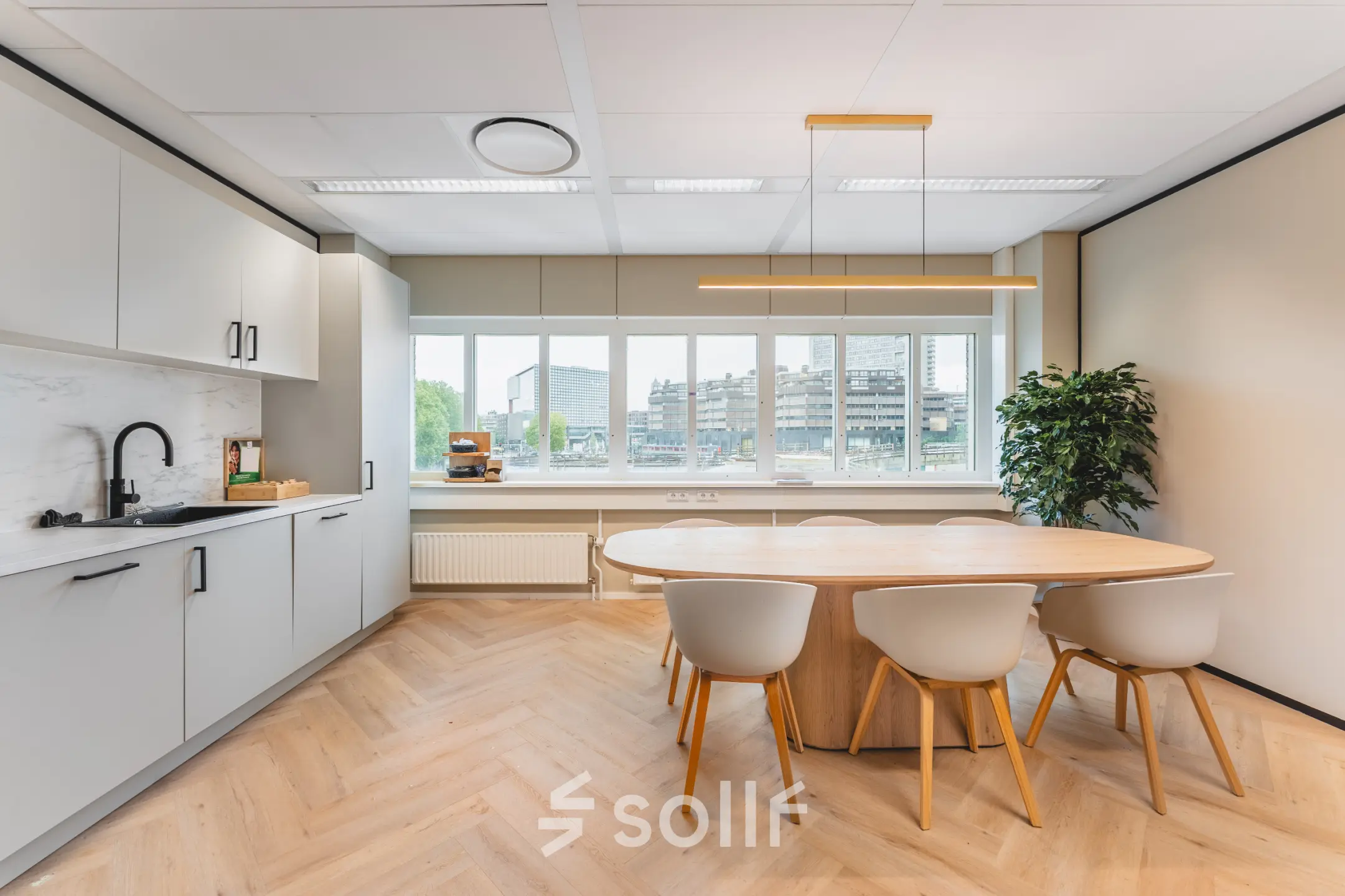 Kantoorruimte met houten vloer en grote ramen bij Utrecht Centraal Station, gelegen op Leidseveer 2-10. De ruimte beschikt over een moderne tafel en keukenblok en biedt een aangename omgeving om te huren.