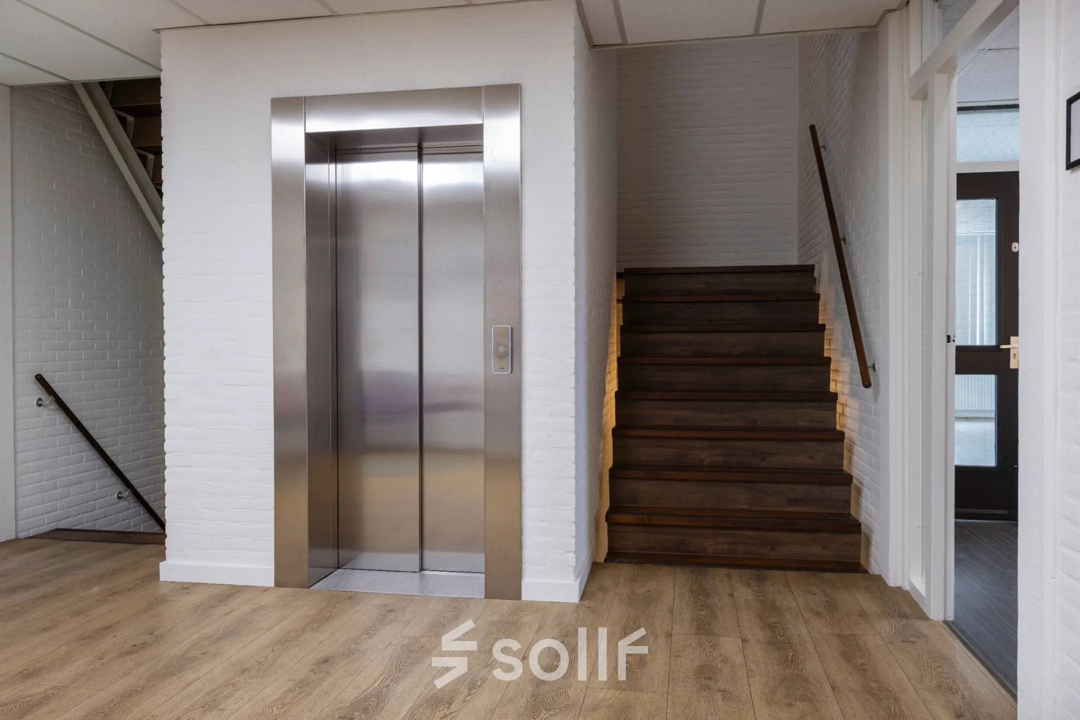 Entree van een kantoorpand met een lift en houten trap, geschikt voor kantoorruimte huren in Utrecht Lage Weide.