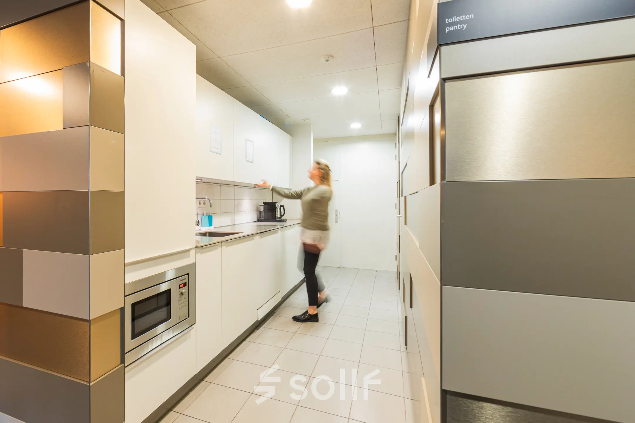 Kantoorruimte huren in Utrecht Leidsche Rijn met een moderne pantry, voorzien van keukenapparatuur waar een persoon een kopje koffie zet.