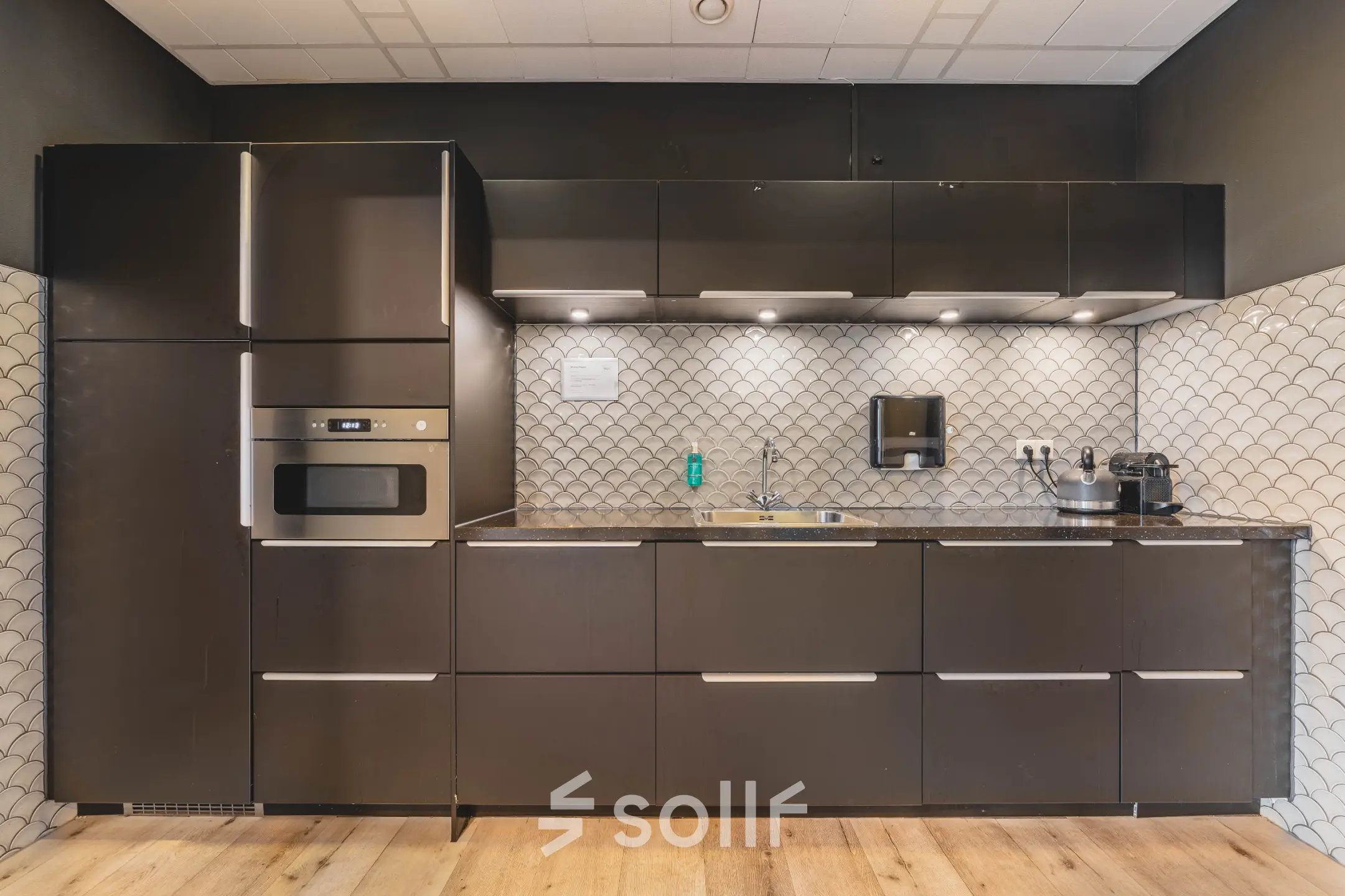 Moderne pantry in kantoorpand gelegen aan de Goeman Borgesiuslaan 77 in Utrecht Noord, met strakke donkerbruine keuken en visgraatmaur. Ideaal voor bedrijven die kantoorruimte willen huren.