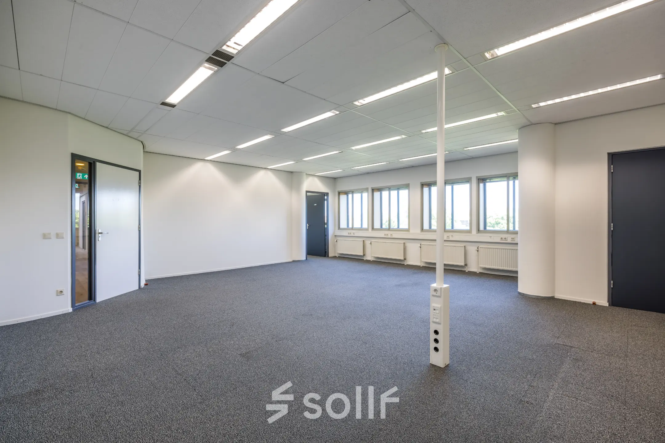 Lichte kantoorruimte in Utrecht Noord met grijze vloerbedekking, grote ramen en twee blauwe deuren langs de wand. Ideaal voor kantoorruimte huren met veel daglicht.
