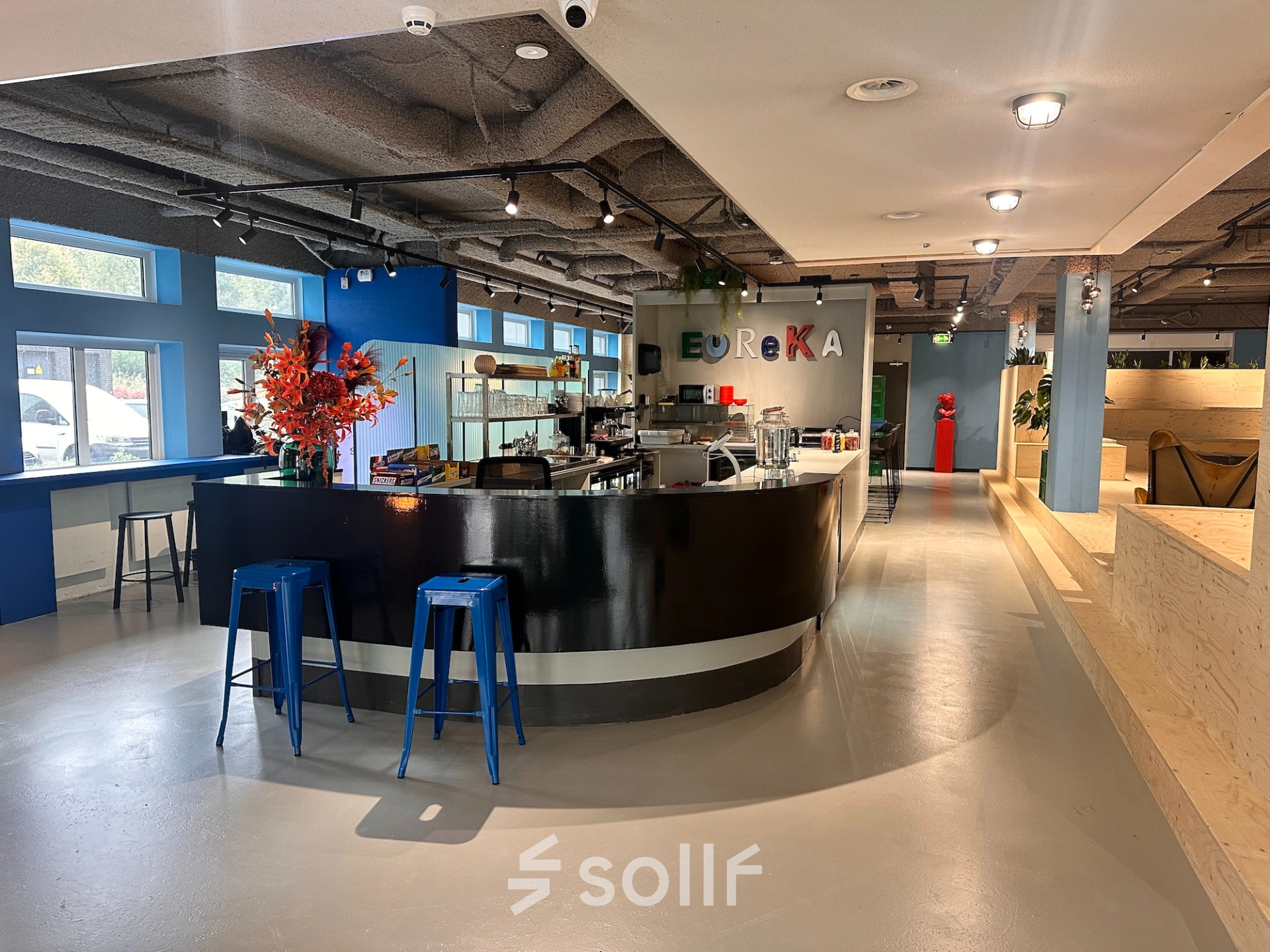 Lichte kantoorruimte huren op Daltonlaan 200 in Utrecht Rijnsweerd met een moderne bar, blauwe krukken en kleurrijke decoraties voor een informele werk- of pauzeomgeving.