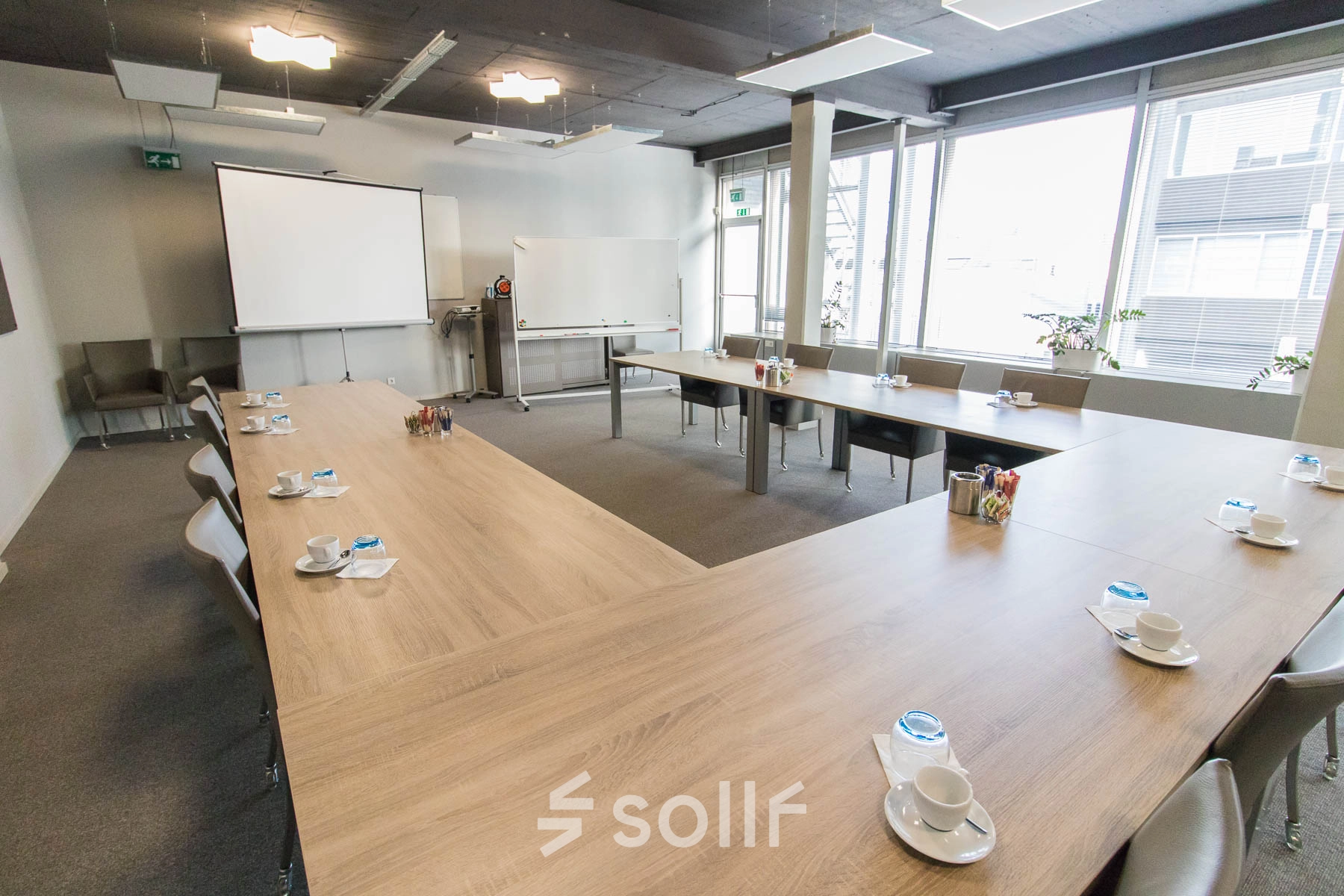 Vergaderruimte met grote tafel op Kaldenkerkerweg 20 in Venlo, ideaal voor kantoorruimte huren. De ruimte is voorzien van projectiescherm, whiteboard en comfortabele stoelen.