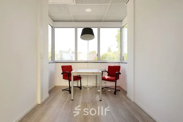 Kantoorruimte huren op Molenweer 2 in Wateringen met twee rode stoelen en een tafel in een lichte ruimte met grote ramen.