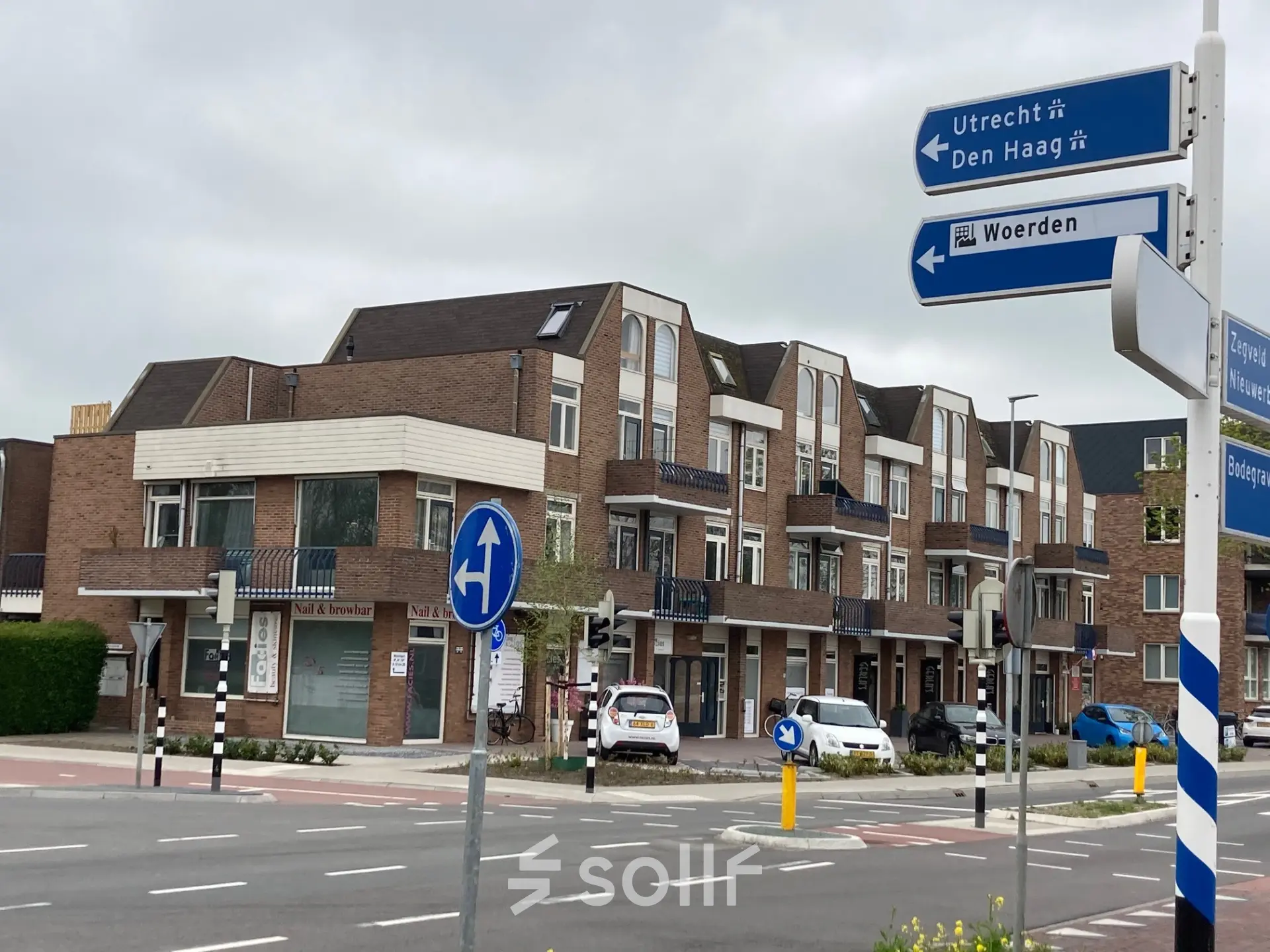 Exterieur van een kantoorpand op Boerendijk 8 in Woerden, gelegen aan een druk kruispunt met verkeersborden richting Utrecht en Den Haag.