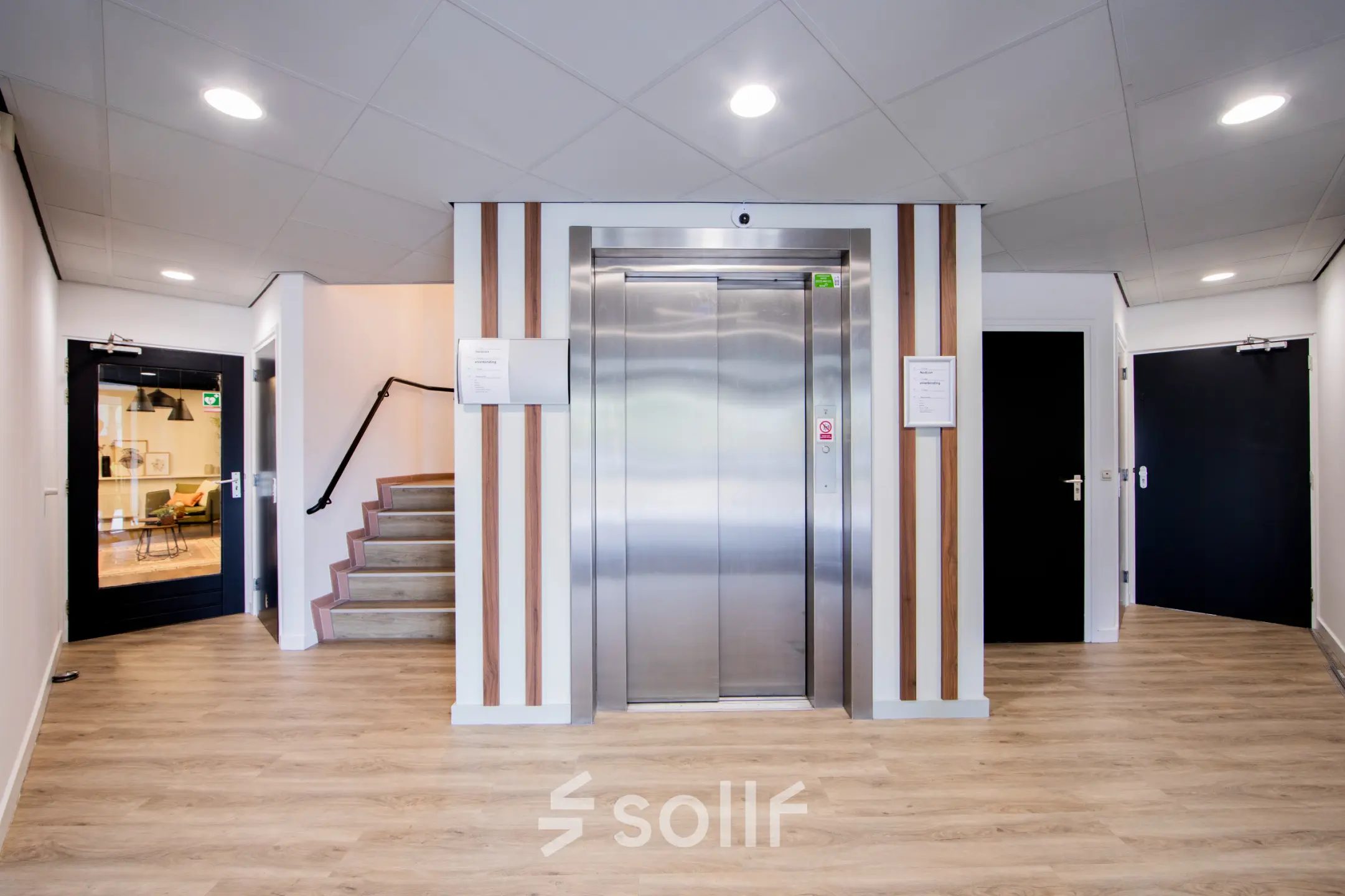 Ingang van een kantoorpand in Woerden op Pelmolenlaan 16, met een lift en trap. Sfeervol verlicht met houten accenten. Kantoorruimte huren mogelijk.