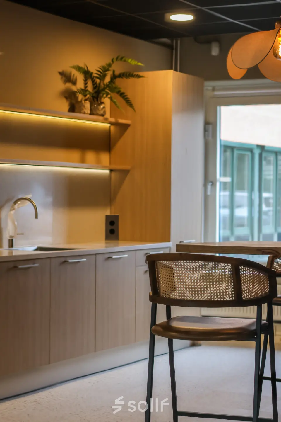 Moderne pantry in een kantoorpand op Vijzelmolenlaan 9, Woerden, met houten keukenkastjes, planten en een stijlvolle hoge stoel aan een bar.
