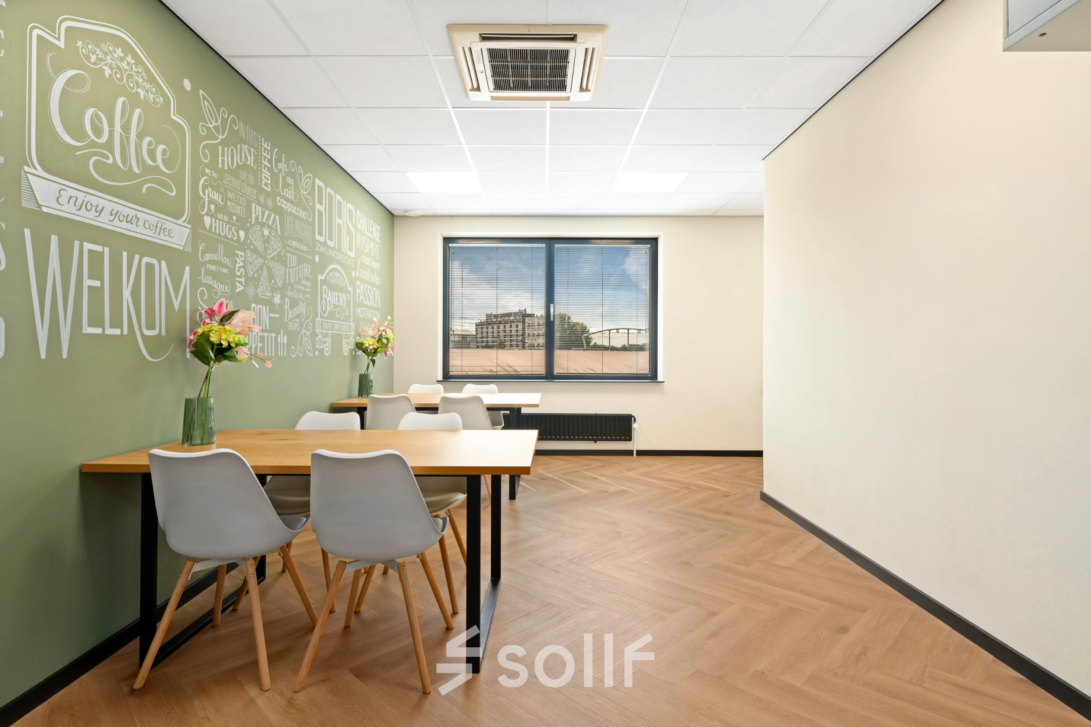 Moderne kantoorpand ingericht als ontmoetingsruimte met houten vloer, groene wanddecoratie en tafel met stoelen. Voor een flexibele kantoorruimte huren in Zwijndrecht, Stationsplein 4.