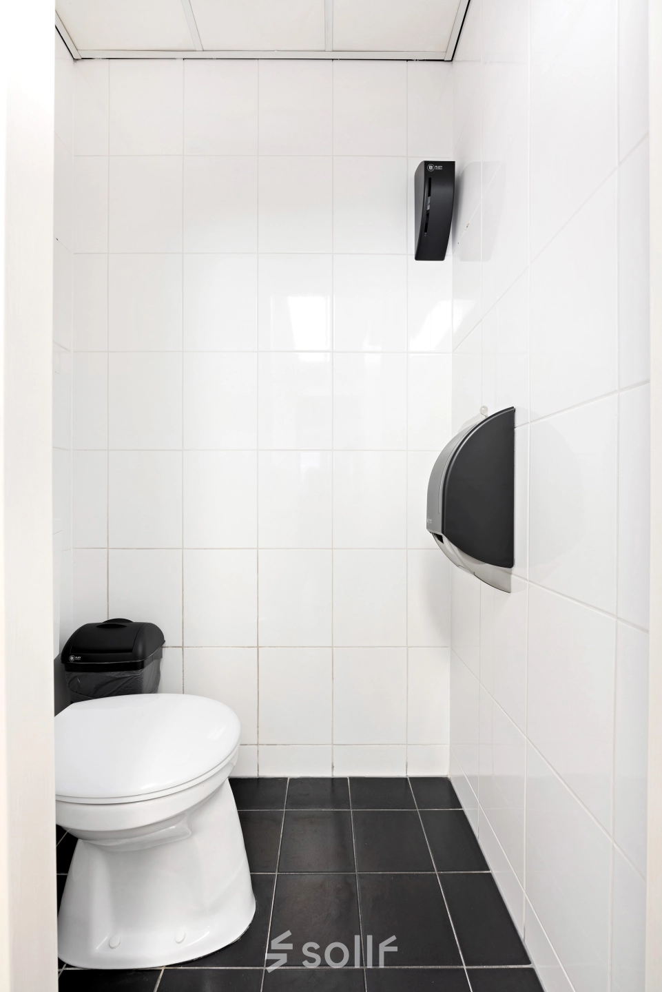 Stijlvolle, wit betegelde toiletruimte met zwarte vloer en moderne voorzieningen in kantoorpand op Stationsplein 4, Zwijndrecht.