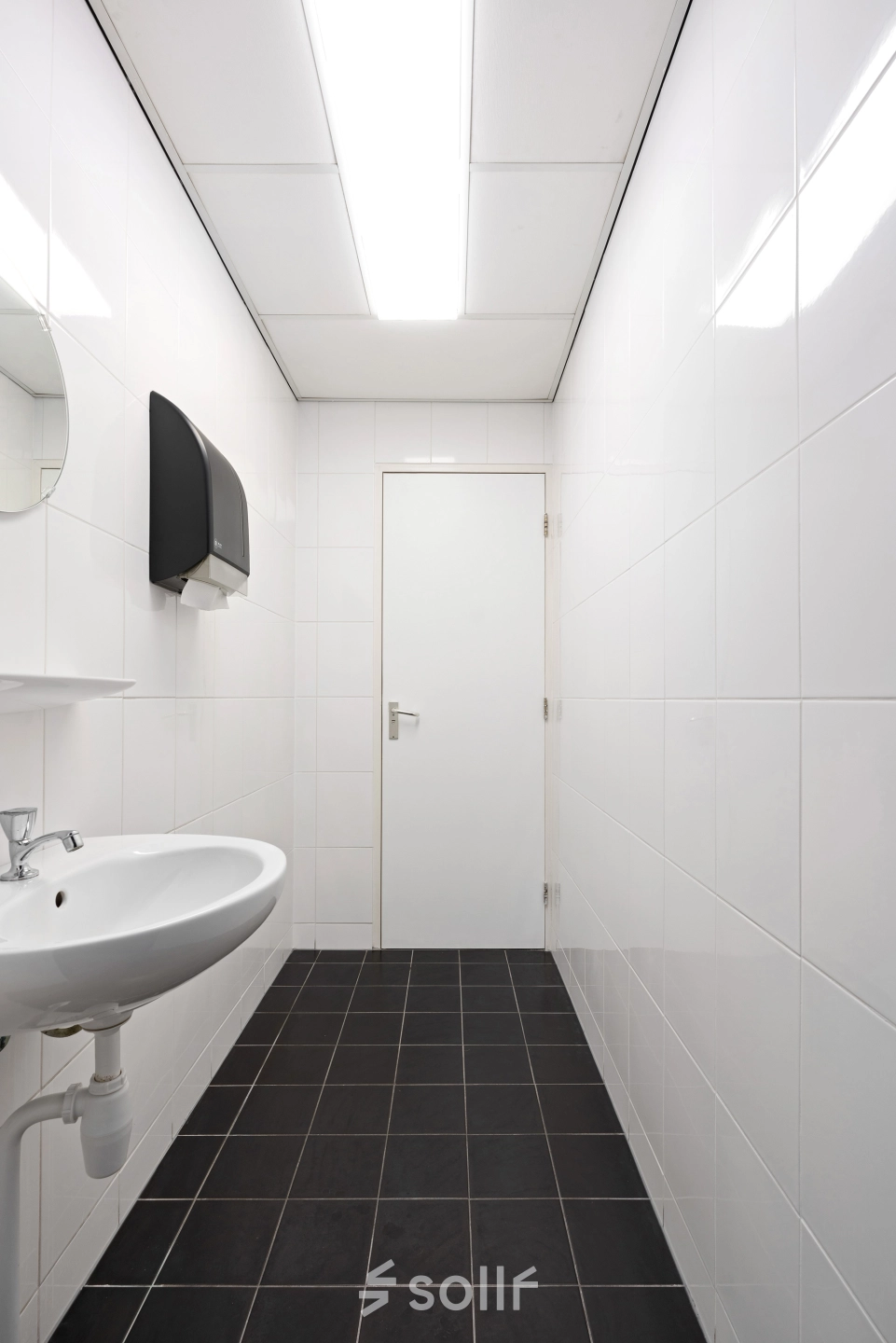 Minimalistische ruimte met witte tegels en wastafel in een kantoorpand aan Stationsplein 4, Zwijndrecht. Ideaal voor bedrijven die kantoorruimte willen huren zonder poespas.