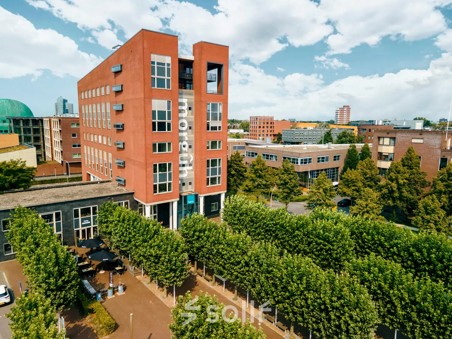 Het kantoorpand aan Hanzeplein 11-27 in Zwolle is omgeven door groene bomen en biedt een moderne uitstraling met een opvallende rode gevel.