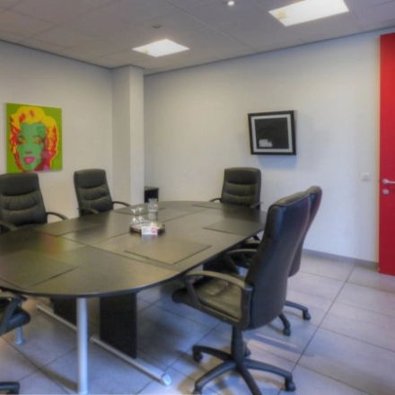 Vergaderruimte met ronde tafel en zes stoelen, kleurrijke kunst aan de muur. Kantoorruimte te huur op Middelmolenlaan 175 in Antwerpen Merksem.