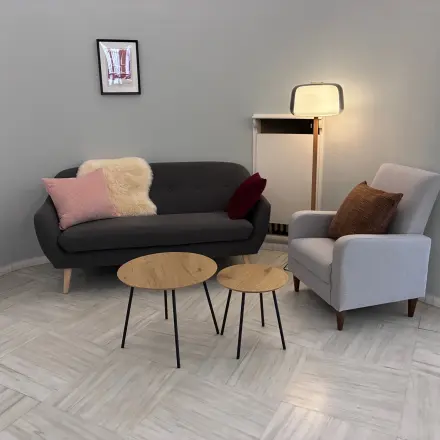 Gezellige loungehoek in kantoor te huur op Avenue Palmerston 3, Brussel Europese Wijk. Grijze zitbank met kussens, bijzettafels en een staande lamp, ideaal voor ontspanningsmomenten.