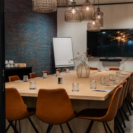 Stijlvolle vergaderruimte met lange tafel, omringd door leren stoelen en verlichte hanglampen. Ideaal kantoorruimte te huur in de Europese Wijk voor professionele bijeenkomsten.