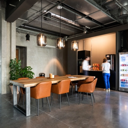 In een modern kantoor op Philipssite 5, Leuven, maken twee personen gebruik van een koffieapparaat en een vergadertafel met leren stoelen. Kantoorruimte te huur biedt volledig gemeubileerde faciliteiten.