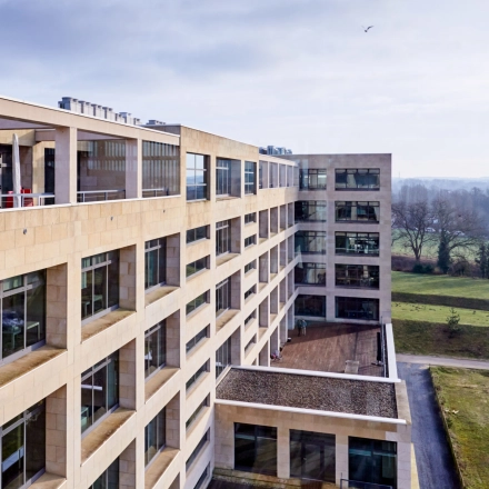 Buitenzijde van een groot kantoor te huur op Philipssite 5 in Leuven met moderne architectuur en veel ramen omgeven door groen.