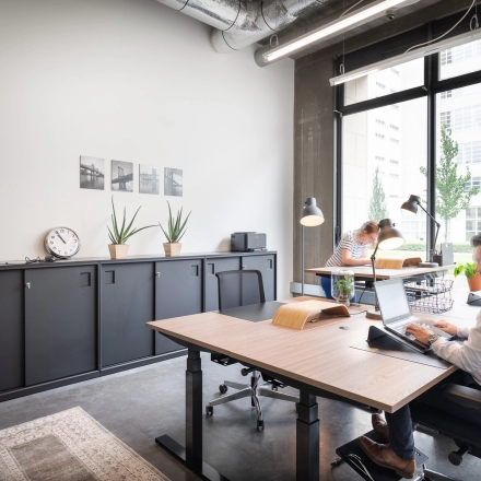 Moderne kantoorruimte te huur in Leuven op Philipssite 5, met strakke meubels en grote ramen die veel licht binnenlaten. Mensen zijn aan het werk, bezig op hun laptops. Ideaal voor wie een kantoorruimte wil huren.