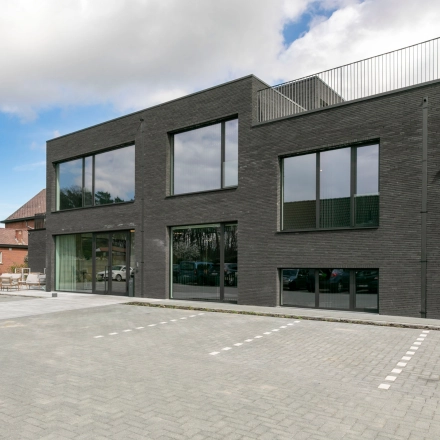 Modern kantoorgebouw te huur aan Olenseweg 375, Westerlo. Stijlvolle gevel met grote ramen, omgeven door parkeerplek. Perfecte locatie voor kantoorruimte huren.