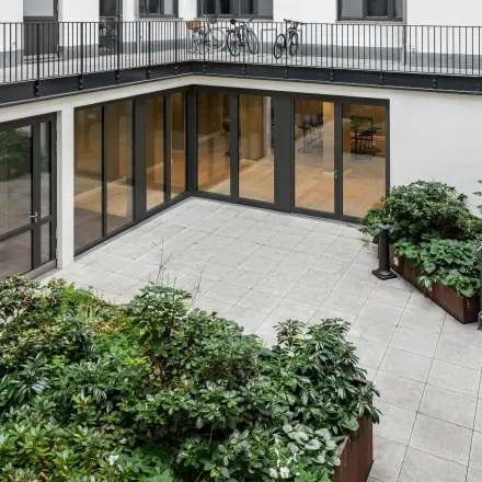 Moderner Innenhof mit Pflanzenbeeten und großen Glasfenstern, die einen Blick in das Bürogebäude an der Chausseestraße 29 in Berlin Kreuzberg bieten.