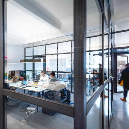 Büroraum mit Glaswänden in der Rudi-Dutschke-Straße 23, Berlin-Kreuzberg, mit arbeitenden Personen an Schreibtischen. Moderne und helle Arbeitsumgebung für Bürofläche mieten.