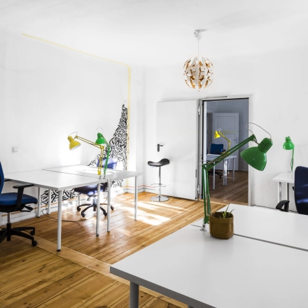 Heller Büroraum in Berlin Lichtenberg mit Holzboden, mehreren Schreibtischen, bunten Lampen und Bürostühlen. Perfekt, um Bürofläche oder Büroraum zu mieten.