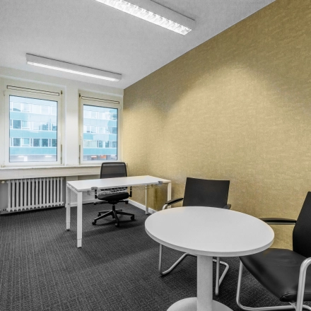 Helles Büro mit zwei schwarzen Stühlen, einem runden Tisch und einem Schreibtisch mit Bürostuhl. Geeignet zum Bürofläche mieten im Düsseldorfer Altstadtviertel.