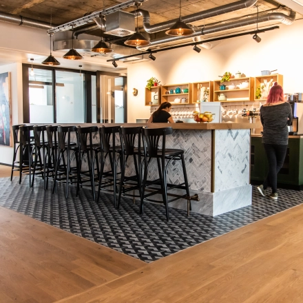 Moderner Büroraum in München Altstadt mit stilvoller Einrichtung und Personen, die an einem Bartresen arbeiten. Perfekte Option, um Bürofläche zu mieten in der Herzogspitalstraße 24.