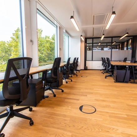 Moderner Büroraum in München Altstadt mit großen Fenstern, Holzfußboden und Schreibtischen; ideal zum Büro mieten und effizientes Arbeiten.