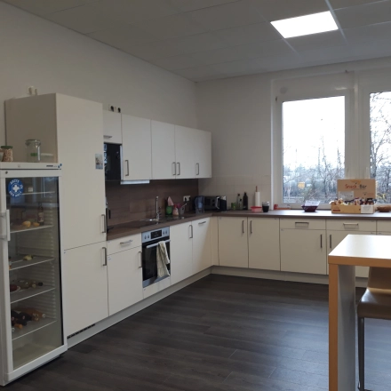 Helle Büroküche zur Miete in München Pasing mit Kühlschrank, Ofen und zwei Barhockern; ideal für Meetings oder Pausen.