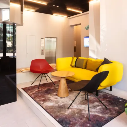 Moderne Empfangslobby mit buntem Sofa und stilvollen Sesseln, ideal für diejenigen, die Bürofläche mieten möchten. Elegante Einrichtung und helle Atmosphäre bieten einen einladenden Raum.