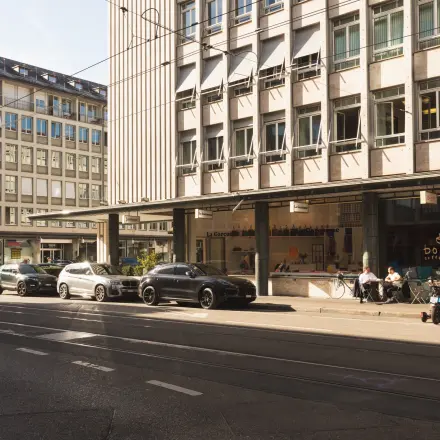 Straßenansicht vor Talacker 41 in Zürich City mit geparkten Autos und Menschen, die sich draußen entspannen. Keine Büros im Bild.