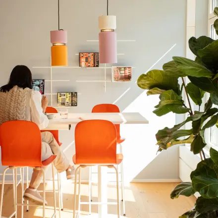 Helles Büro mit hohen Tischen und orangefarbenen Stühlen in Zürich City, ideal für kreativen Austausch. Person im Gespräch.
