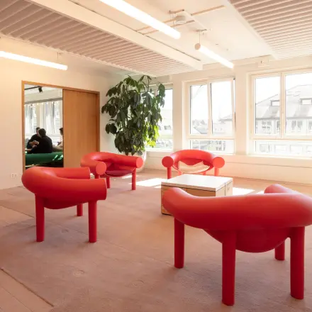 Helles Büro in Zürich City mit roten Sitzgelegenheiten und großen Fenstern, ideal zur Miete als Büroraum mit möbliertem Interieur.