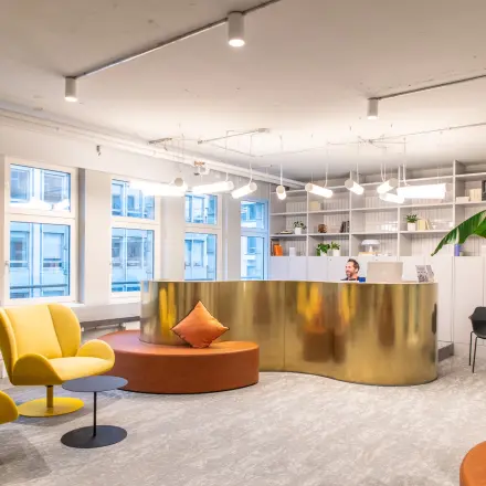 Modernes Büro in der Uraniastrasse 31, Zürich City, mit stilvollen Möbeln, auffälliger goldener Rezeption und Pflanzen. Eine Person empfängt Besucher.