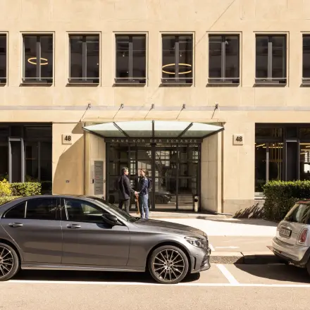 Außenansicht des Büros in der Beethovenstrasse 48, Zürich Enge. Zwei Personen stehen vor dem Eingang, parkende Autos davor.