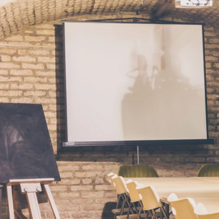 Interior of a furnished office space at Zimmermanngasse 8, 1090 Vienna, featuring a long table with chairs, a projector screen, and a flip chart, ideal for office space rental.