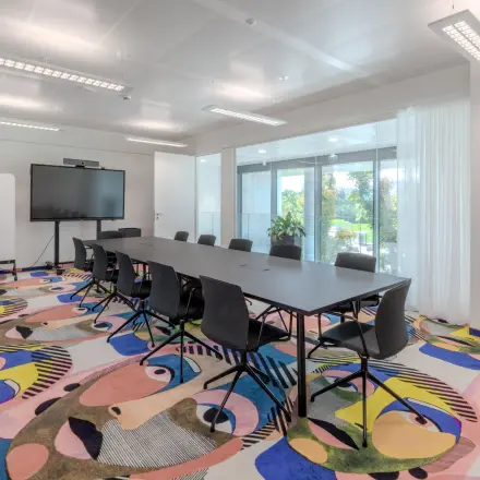 Bright office space in Siemensstraße 89, 1210 Vienna with colorful carpet, long conference table, and large screen; ideal for office space rental.