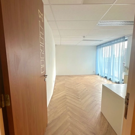 Interior view of an office space at Hollandse Kade 38, Abcoude, ideal for office space rental, featuring wooden flooring, white walls, and large windows with blue curtains.