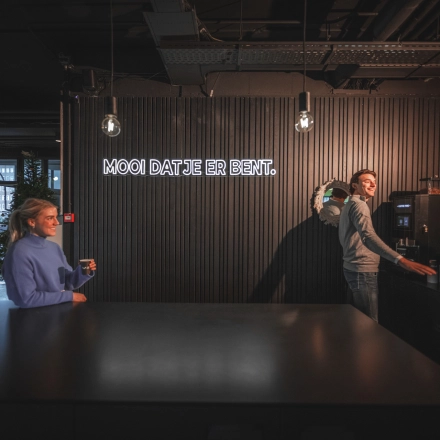 Two people in a modern office space at Egbert Gorterstraat 2-14, Almelo, enjoying coffee near a sleek counter with ambient lighting, ideal for informal meetings. Office space rental available in this vibrant location.