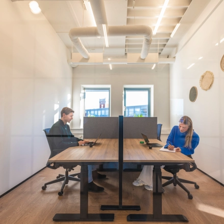 Bright office space in Almelo at Egbert Gorterstraat 2-14 featuring two people working at desks, ideal for office space rental. Modern design with large windows and stylish décor, providing a productive environment.