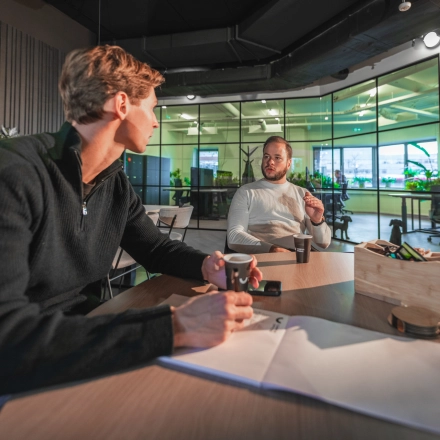 Two professionals engaged in a business discussion at a modern, furnished office space at Egbert Gorterstraat 2-14, Almelo. The bright interior creates an ideal environment for office space rental.