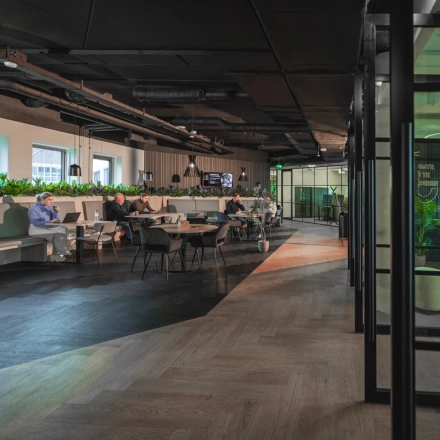 Spacious office interior at Egbert Gorterstraat 2-14 in Almelo, featuring modern workspaces with seating areas, plants, and individuals engaged in business activities. Ideal office space rental for dynamic professionals.