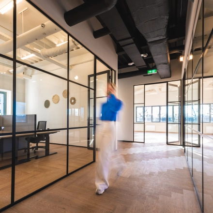 Modern office interior featuring glass partitions and wooden flooring in Egbert Gorterstraat 2-14, Almelo. Sleek design enhances work environments for office space rental, with visible workstations and natural lighting.