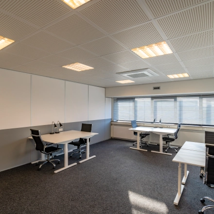 Modern workspace at Transistorstraat 151, featuring several desks and chairs, ideal for office space rental in Almere Poort. The room is well-lit with large windows and simple decor.