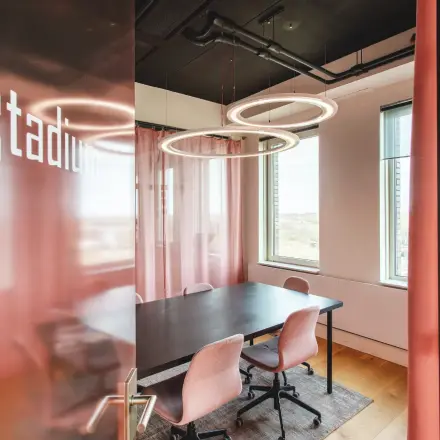 Furnished office space with a black table and pink chairs available for rent at Landdrostdreef 124, Almere Stad. Large windows provide ample natural light.