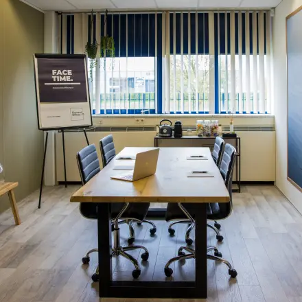 Modern meeting room with wooden table, leather chairs, flip chart, and a laptop. Ideal office space rental in Almere Stad for collaborative work.