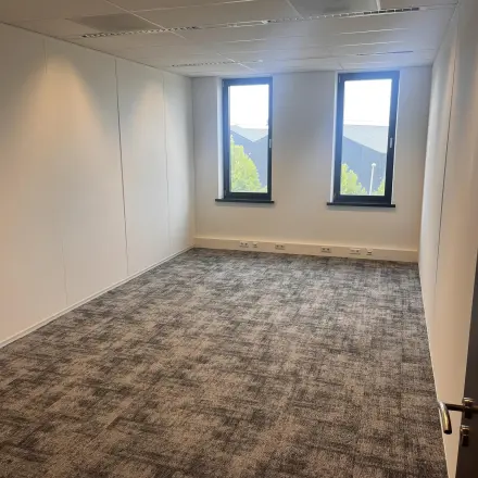Empty office space with carpet flooring and two windows at Leidse Schouw 2 for rent in Alphen aan den Rijn.