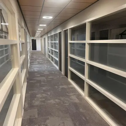 Long hallway with carpeted floor and glass partition walls in an office space for rent at Leidse Schouw 2, Alphen aan den Rijn.